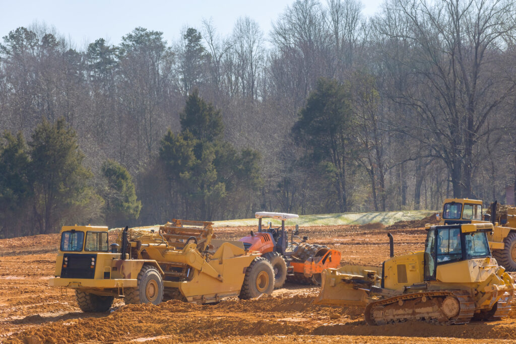 Construction site with heavy equipment performing grading and earthwork takeoffs, preparing cut and fill areas based on site plans and volume estimates.