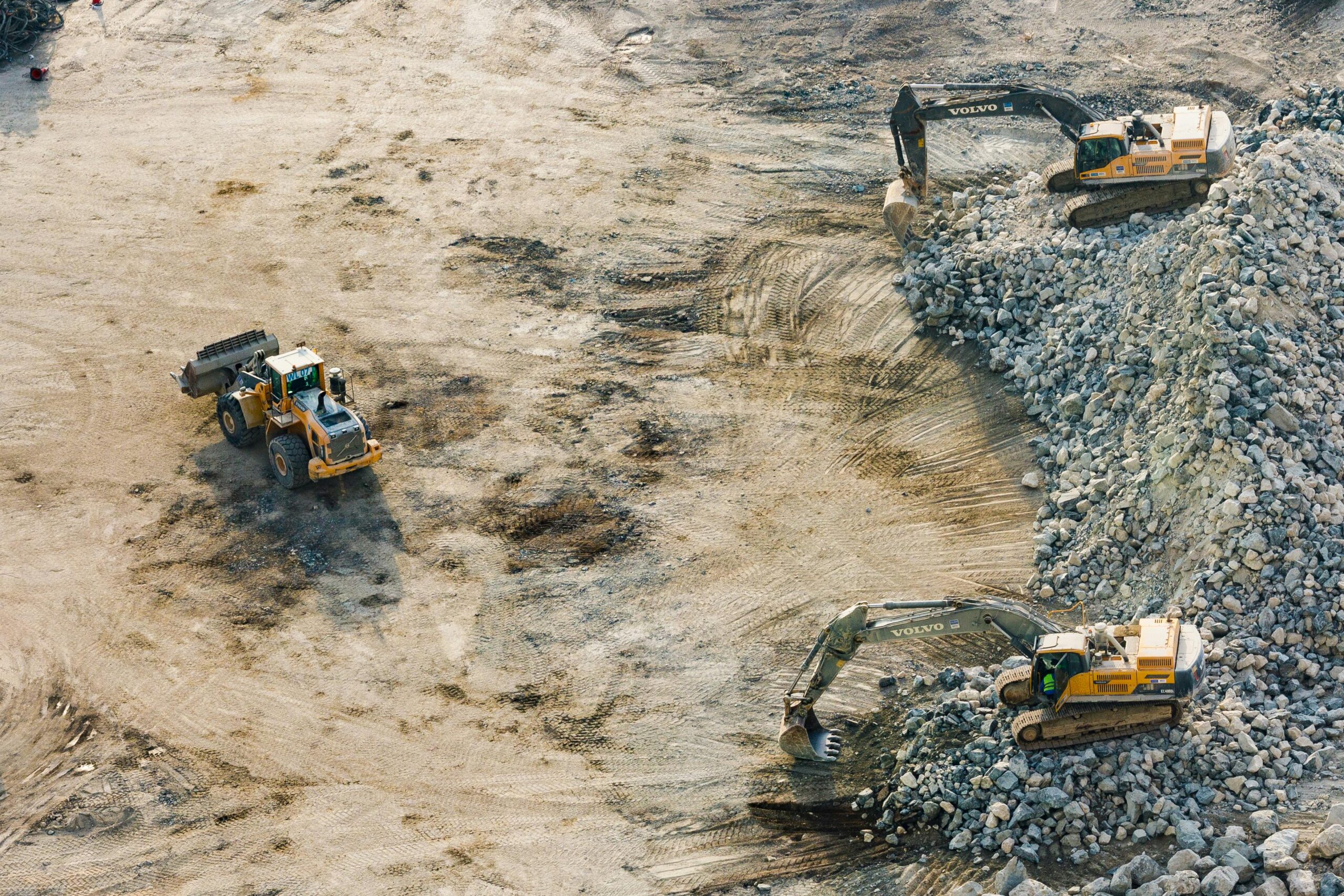 "A split-screen image showcasing construction machine control technology: on the left, a bulldozer leveling soil at a construction site under a clear sky; in the center, a digital display showing real-time 3D terrain data for machine control; on the right, an excavator performing precise grading work in a similar outdoor setting."
